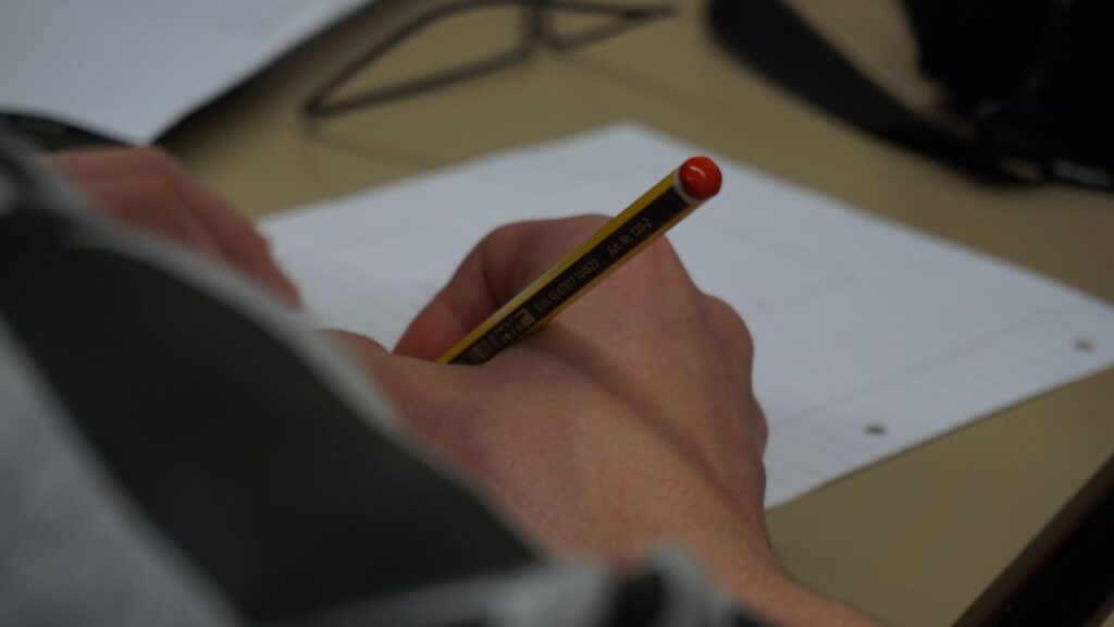 Hand holding a pencil writing on lined paper indoors