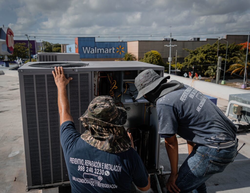 Two technicians repair a rooftop HVAC unit outside a Walmart store.
